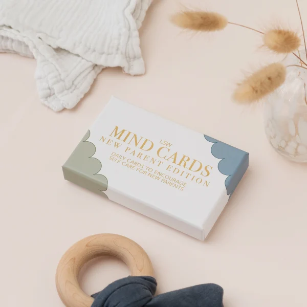 Mind Cards: New Parent Edition box beside a wooden teething ring and a muslin cloth