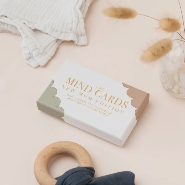 Mind Cards: New Mum Edition box beside a wooden teething ring and a muslin cloth